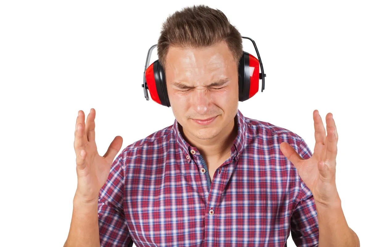 Man wearing red ear defenders with his eyes squeezed shut