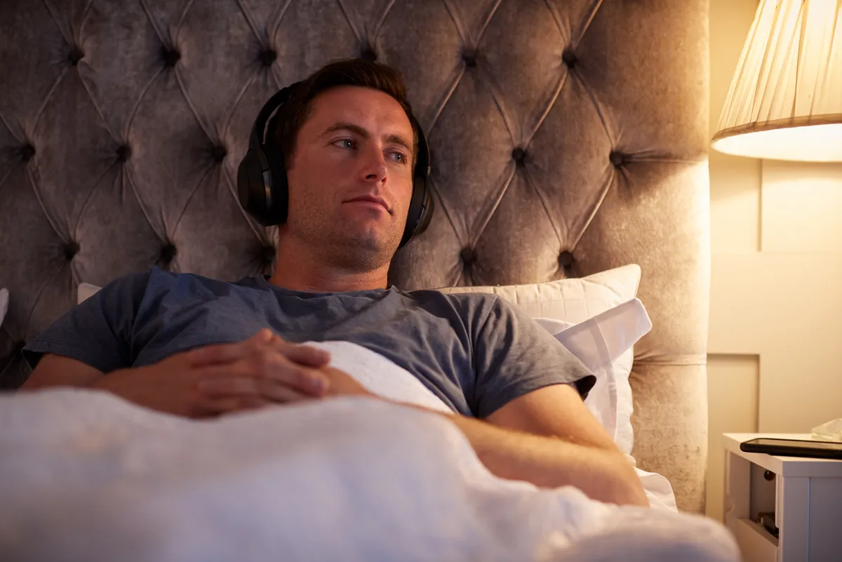 Man lying in bed at night wearing wireless over-ear headphones
